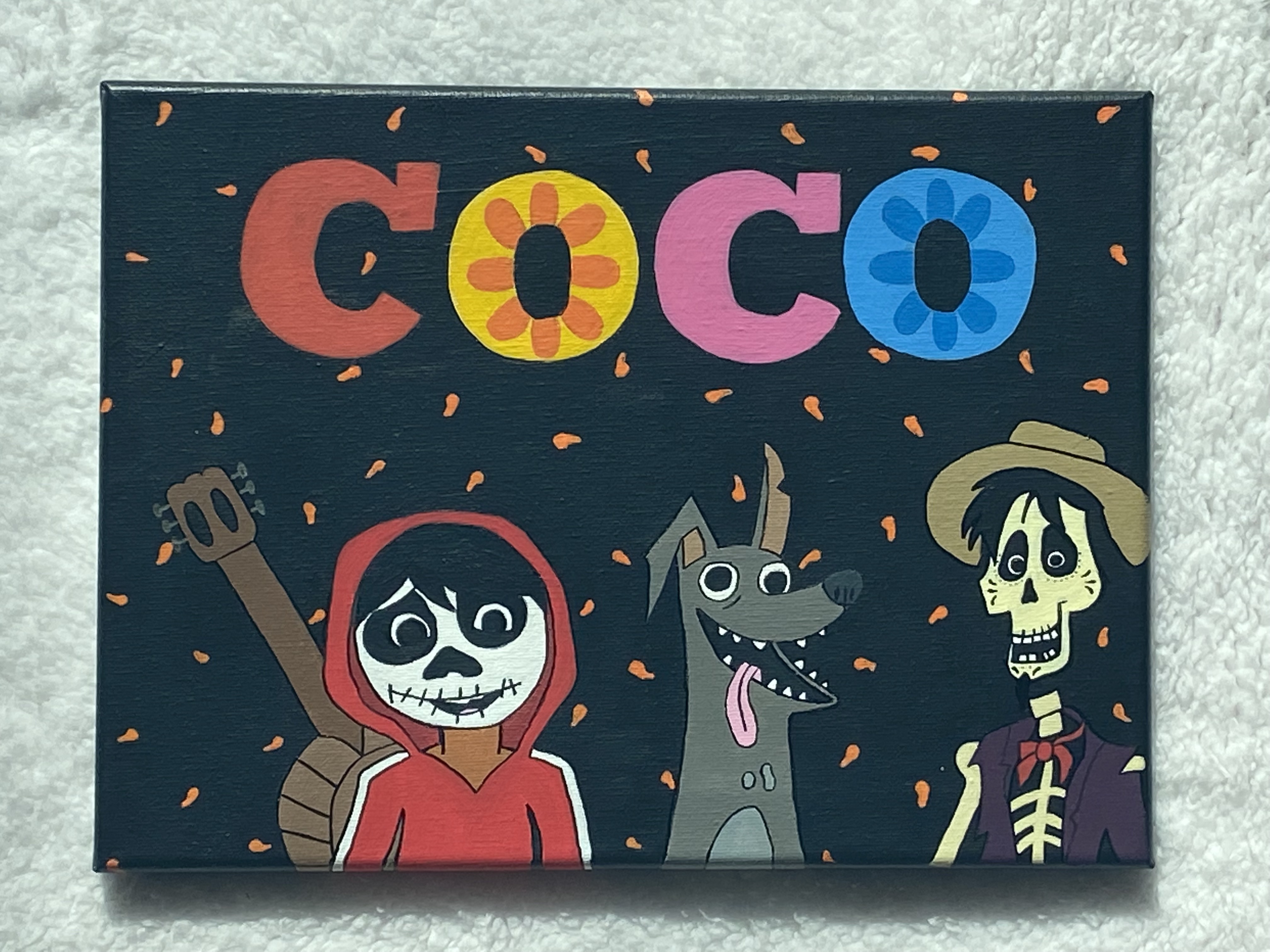 Miguel, Dante, and Hector from Coco surrounded by orange marigold petals. The title Coco is painted above them.