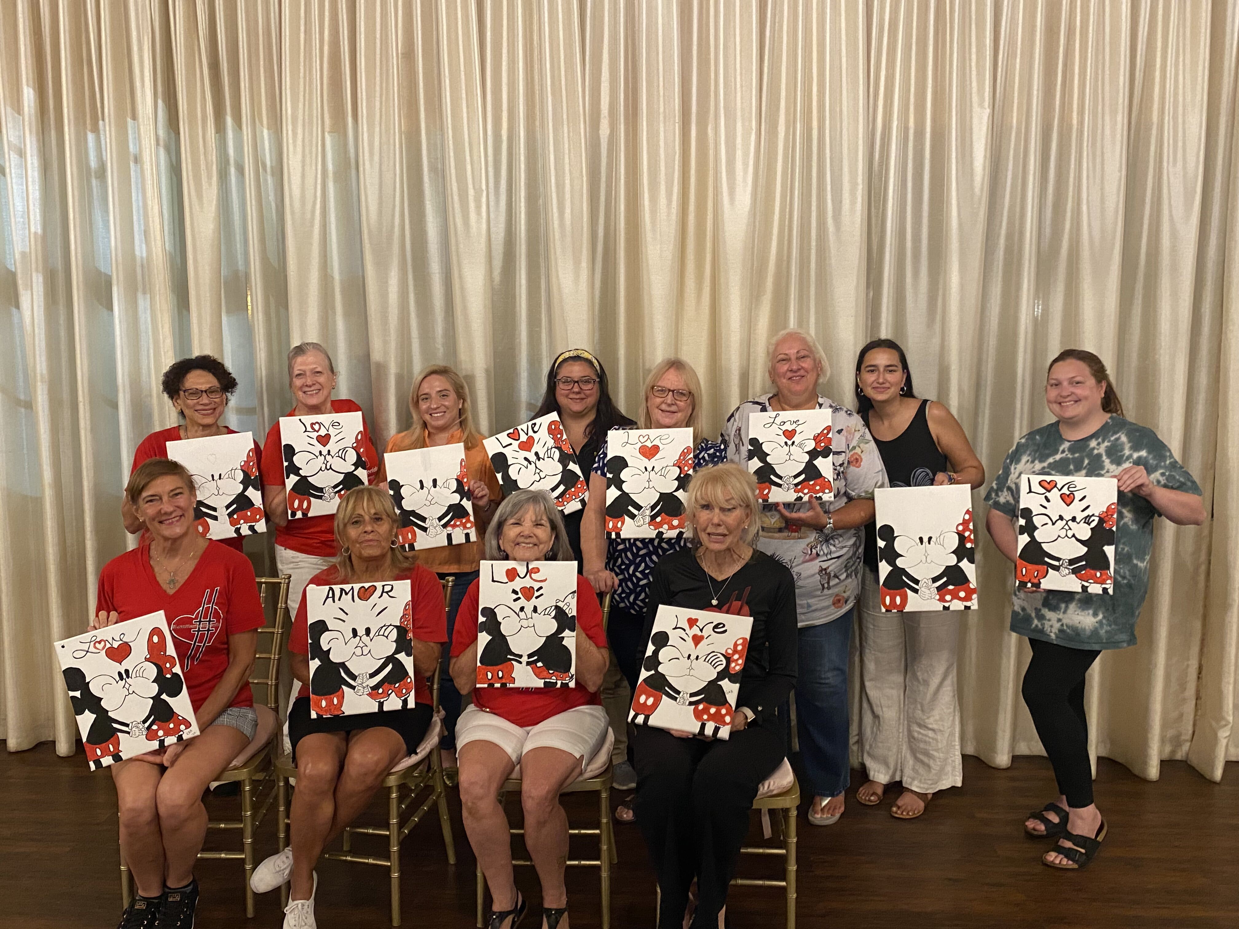 A group of women holding paintings of Mickey and Minnie.