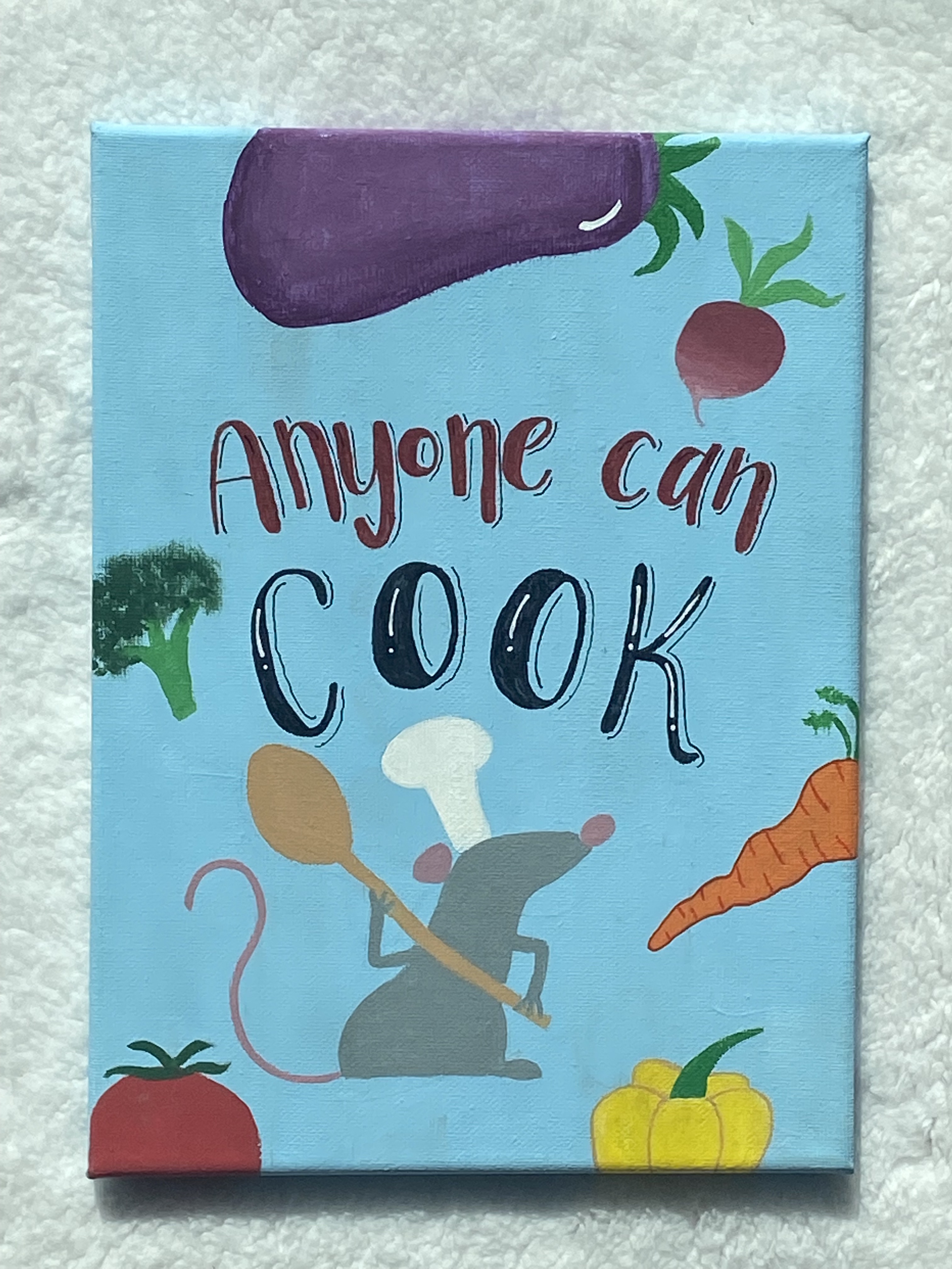 Remy, a gray rat wearing a chef's hat and holding a spoon, stands besides vegetables to say Anyone can cook.